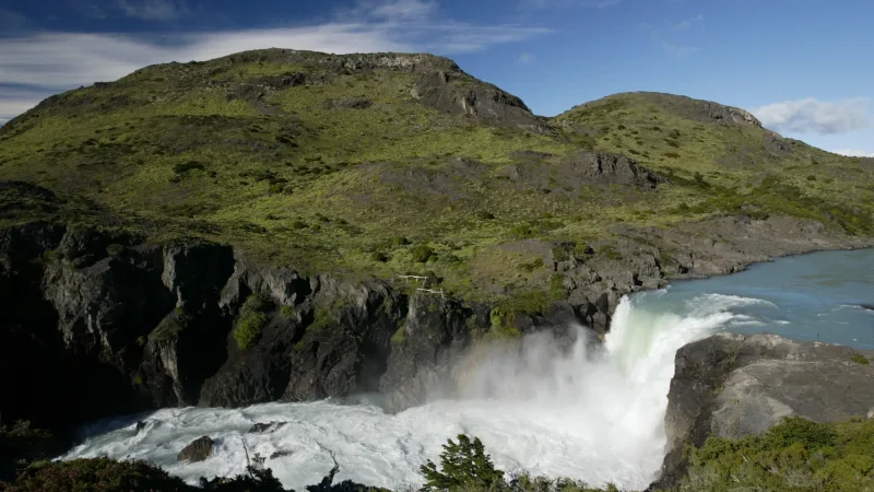 Água branca e espumosa caindo em cascata da borda do Salto Grande, com picos distantes ao fundo.