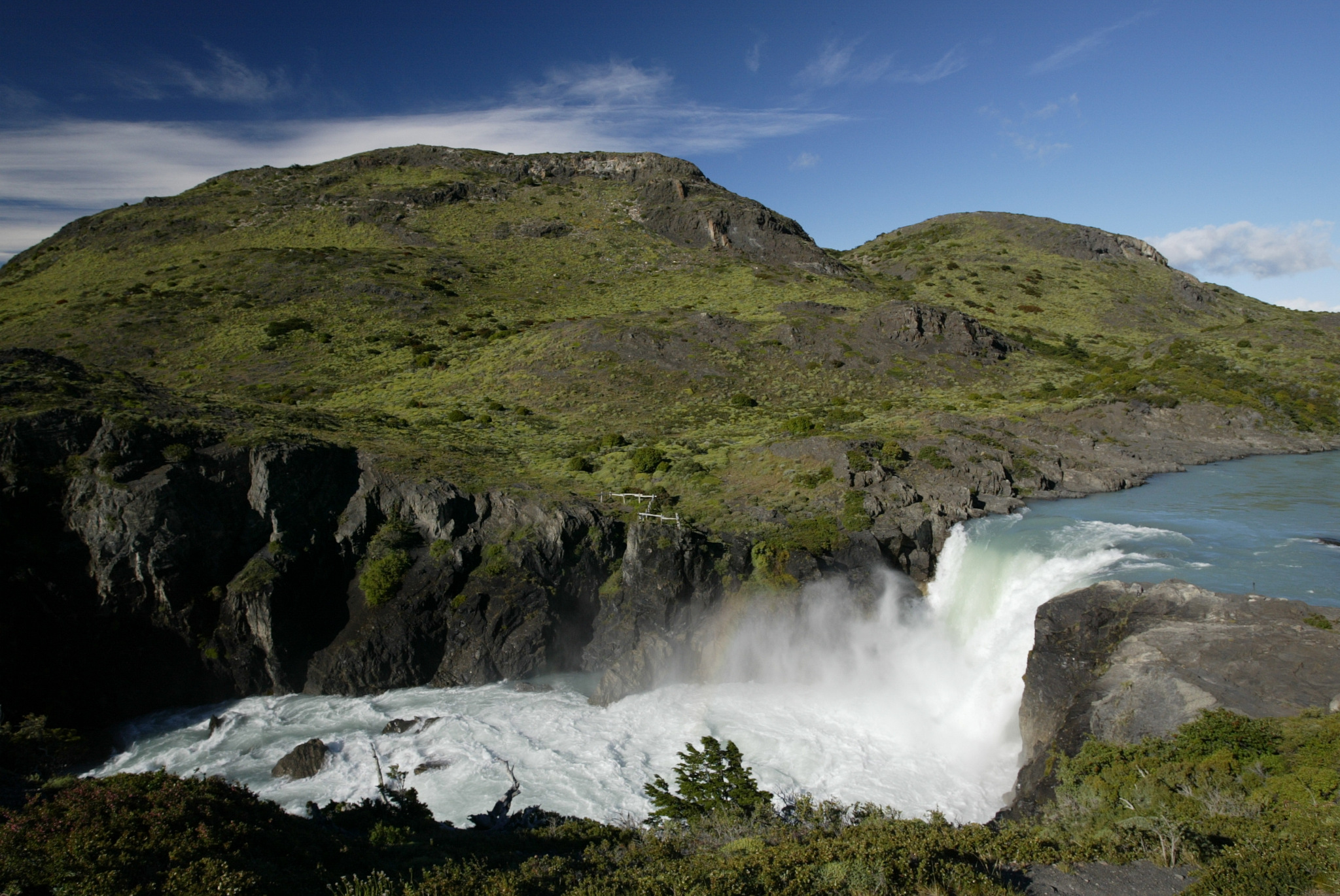 Agua blanca y espumosa cayendo en cascada sobre el borde del Salto Grande, con picos lejanos al fondo.
