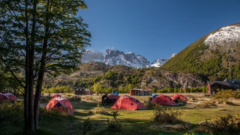 Vibrant hiking tents scattered across the green meadows near the edge of Lago Dickson.