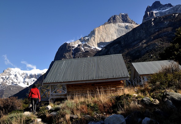 The rustic wooden exterior of Refugio Los Cuernos with the granite peaks of the massif in the background.