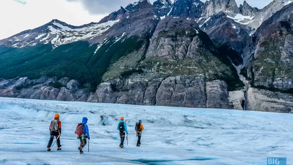Adventurous hikers wearing crampons while walking across the blue ice of a Patagonian glacier.