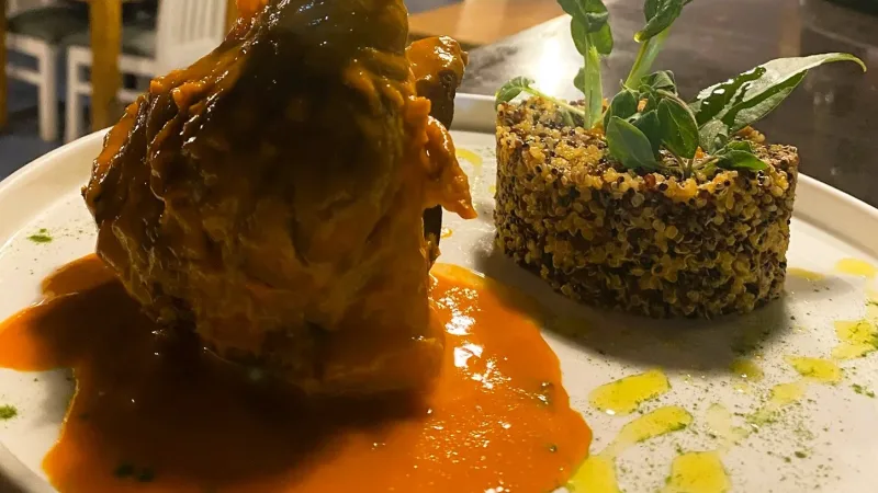 Pernil de cordeiro ao molho com quinoa e ervas em prato branco, no restaurante La Cuisine em Punta Arenas