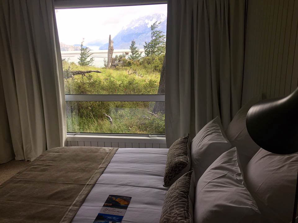 Panoramic exterior of Hotel Lago Grey with the greyish waters of the lake and the glacier in the background.