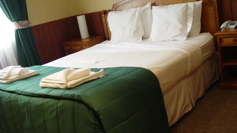 Quarto duplo standard no Hotel Martin Gusinde com roupa de cama limpa e iluminação interior aconchegante.