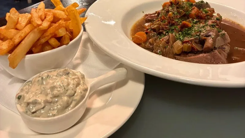 Prato de carne com legumes, batatas fritas e molho no restaurante La Cuisine, com paredes decoradas com frases em francês