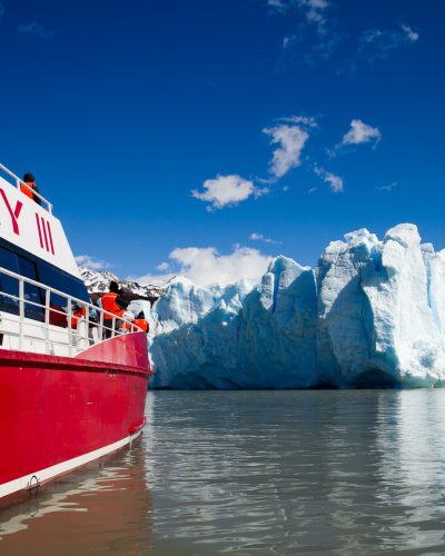 Um enorme iceberg azul flutuando no Lago Grey, com o campo de gelo da geleira visível ao longe.