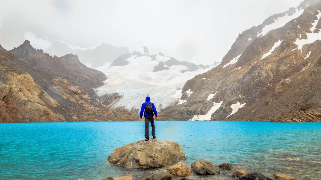 Un excursionista solitario con una mochila está de pie en una cresta, contemplando la vasta cordillera.