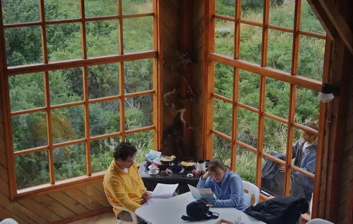 Las cabañas rústicas con estructura en forma de A y el albergue principal del Refugio Los Cuernos junto al lago.