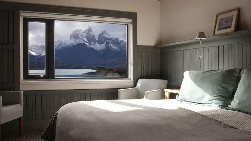 Uma suíte de luxo com cama king-size no Hotel Explora, com janela que oferece vista direta para os Cuernos del Paine.