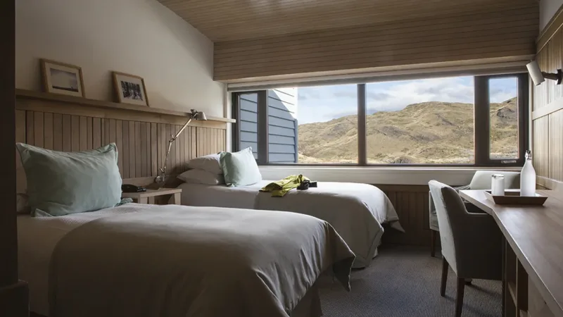 Quarto de hóspedes com duas camas de solteiro no Hotel Explora, com painéis de madeira minimalistas e vista para a cachoeira Salto Chico.