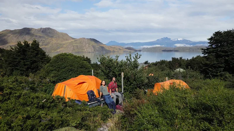 Tiendas de campaña instaladas sobre plataformas de madera en el Camping Los Cuernos, rodeado de densos bosques y picos montañosos.