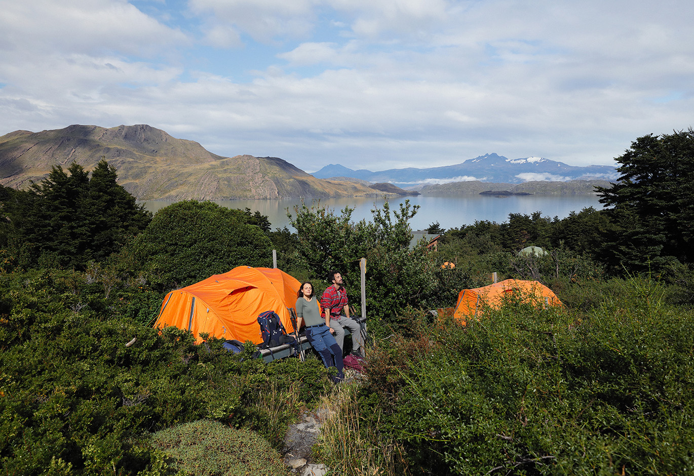 Tents pitched on wooden platforms at Camping Los Cuernos, surrounded by dense forest and mountain peaks.