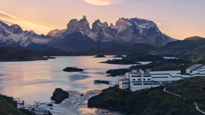 Vista exterior da arquitetura branca e discreta do Hotel Explora Patagonia sob um céu limpo.