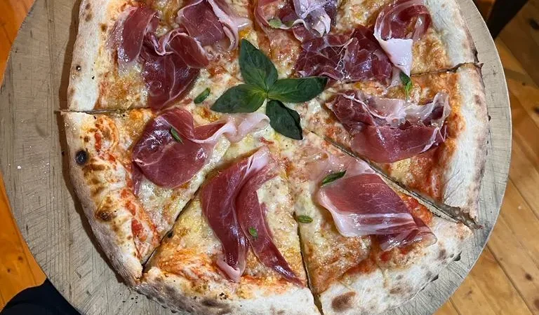 Una pizza fresca hecha en horno de leña con varios ingredientes, servida sobre una tabla de madera.