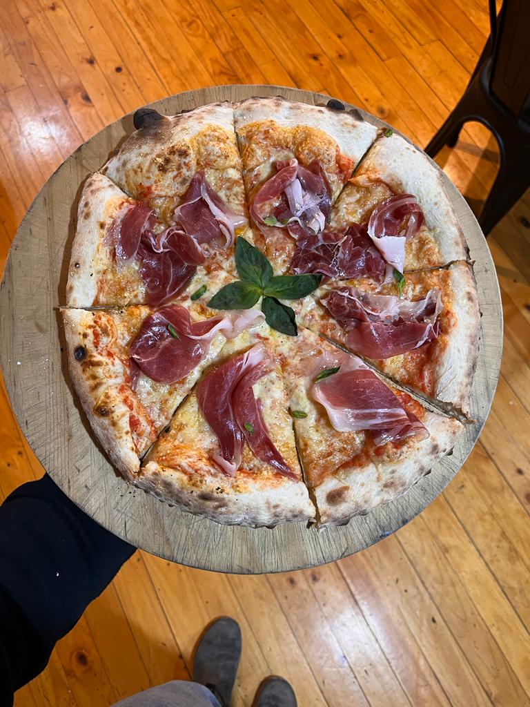 Una pizza fresca hecha en horno de leña con varios ingredientes, servida sobre una tabla de madera.