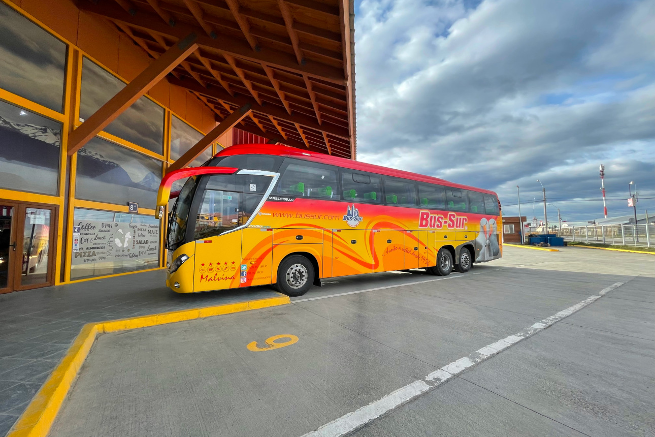 Travelers collecting their luggage from the underside compartment of a Bus Sur coach.
