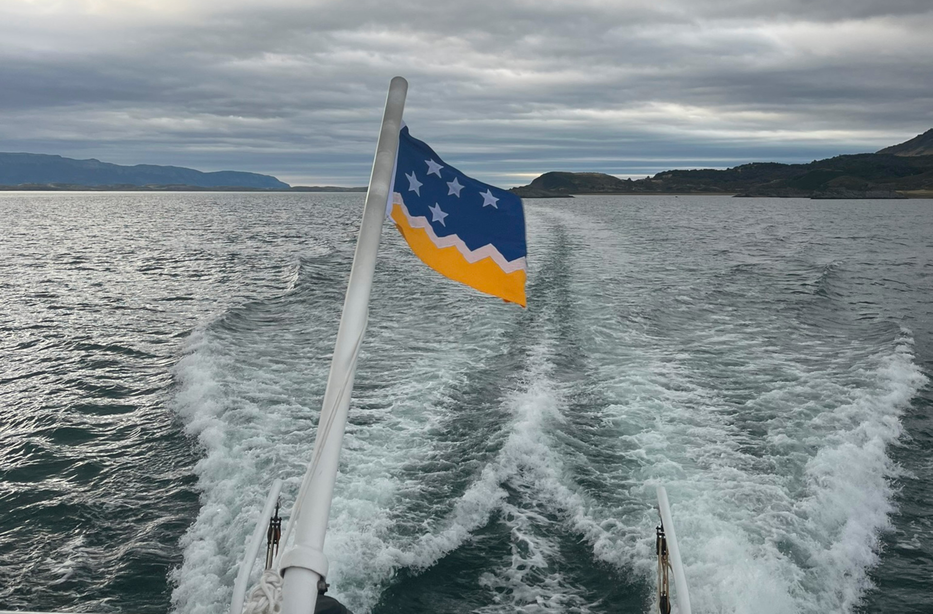 A group of tourists wearing life jackets on a boat approaching a large glacier.