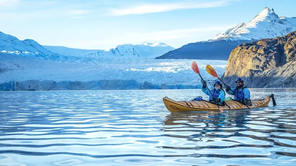 Kayakers in bright red kayaks paddling through the icy turquoise waters of Lake Grey near a glacier.