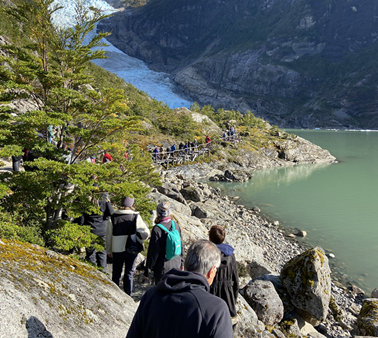 Grupo de visitantes caminando por sendero rocoso hacia el glaciar Serrano, con lago glaciar turquesa y montañas nevadas al