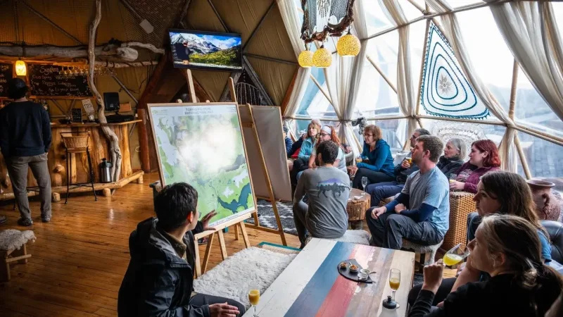 Guide presenting a Torres del Paine National Park map to guests inside an EcoCamp Patagonia geodesic dome lounge