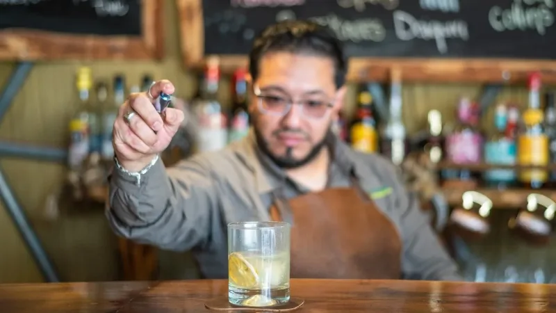 Bartender adding finishing touches to a cocktail with lemon slice at EcoCamp Patagonia's rustic bar