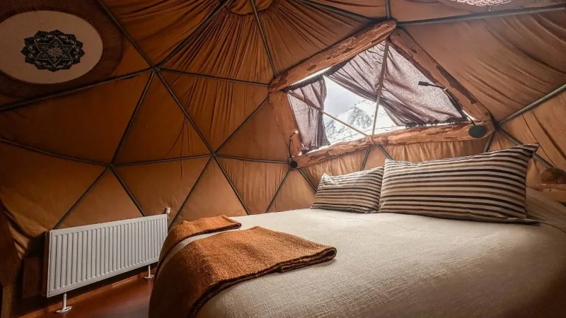 Cozy geodesic dome interior at EcoCamp Patagonia with a double bed, striped pillows, and a window revealing snowy peaks