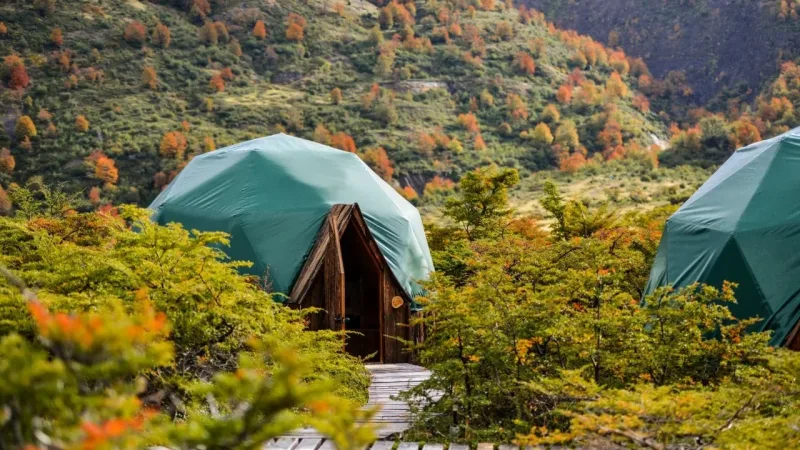 Teal geodesic dome tents nestled among autumn foliage on a Patagonian hillside at EcoCamp Patagonia