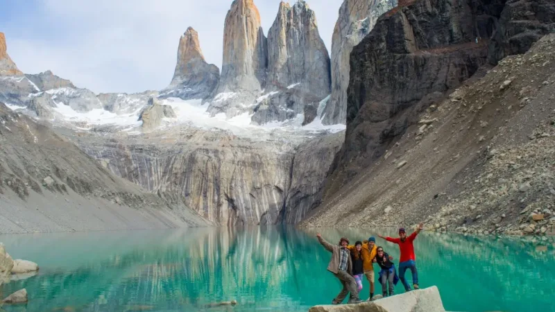 Group of hikers posing beside a turquoise lake with the iconic Torres del Paine granite towers in Patagonia, Chile