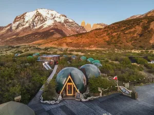 Domos geodésicos del EcoCamp Patagonia rodeados de vegetación, con las Torres del Paine y montañas nevadas al fondo.