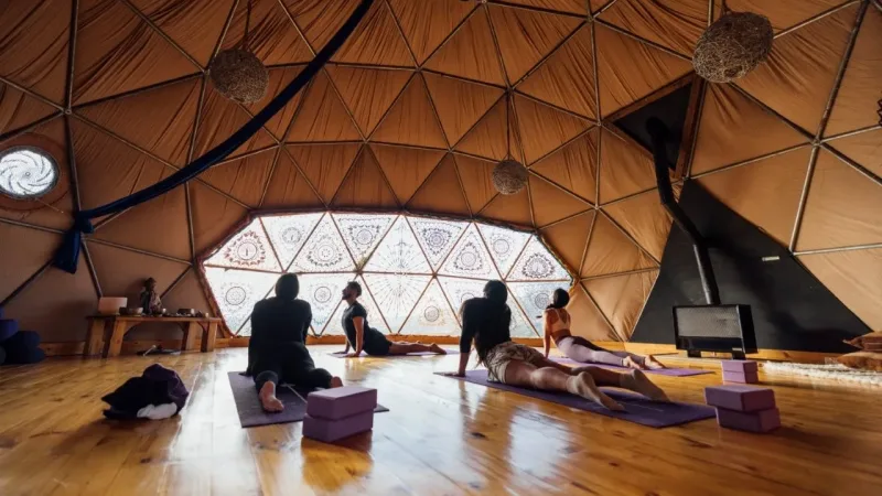 People practicing yoga on mats inside a geodesic dome tent with warm wooden floors at EcoCamp Patagonia