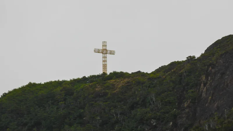 Cruz metálica dorada en la cima del Cabo Froward, rodeada de vegetación patagónica bajo un cielo gris