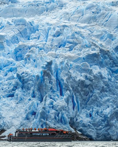 Embarcación con turistas frente a la imponente pared de hielo azul del Glaciar Sarmiento en la Patagonia chilena.