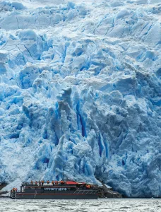 Embarcación con turistas frente a la imponente pared de hielo azul del Glaciar Sarmiento en la Patagonia chilena.