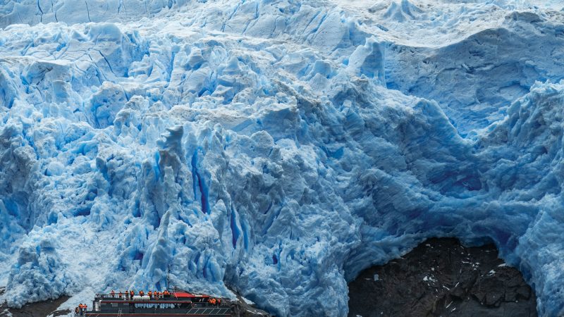 Embarcación con turistas frente al imponente muro de hielo azul del glaciar Sarmiento en Patagonia