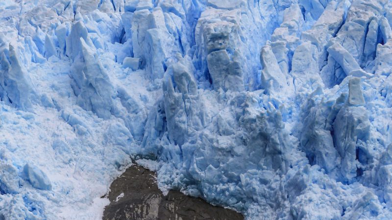 Frente del Glaciar Sarmiento con torres de hielo azul sobre roca oscura y agua gris en primer plano