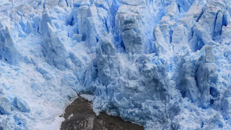 Frente del Glaciar Sarmiento con torres de hielo azul sobre roca oscura y agua gris en primer plano